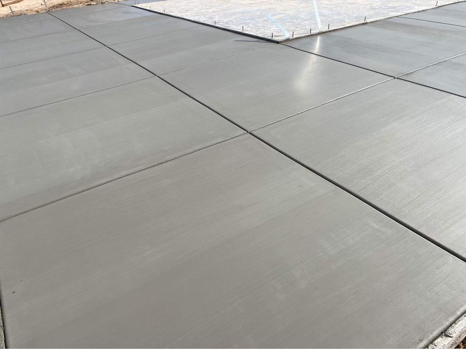 Freshly poured and smoothed concrete slabs by expert concrete contractors form a large, flat surface in Riverside CA, divided into square sections with visible seams. The cement appears uniformly gray and reflective under daylight, indicating recent work completion.