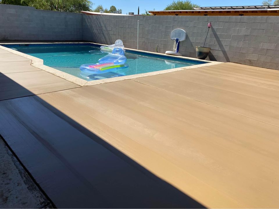 In Riverside, CA, a backyard pool features a clear inflatable lounge float and a custom-designed basketball hoop at the edge. Surrounded by a tall privacy wall, the pool area boasts a sleek concrete pool deck, where bright sunlight dances across the patio's surface.