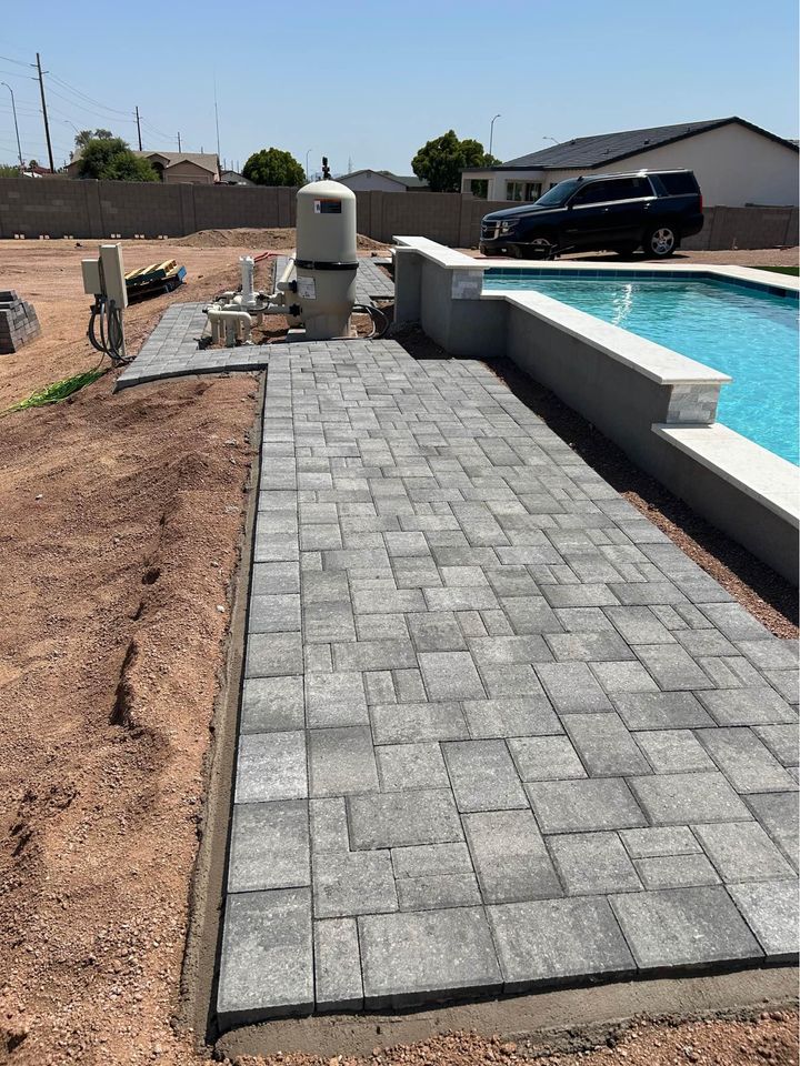 A newly paved walkway with gray stone tiles enhances the outdoor living space as it runs alongside a swimming pool in a sunny Riverside, CA backyard. In the background, a black SUV is parked near the edge of the property, hinting at expert paver installation.